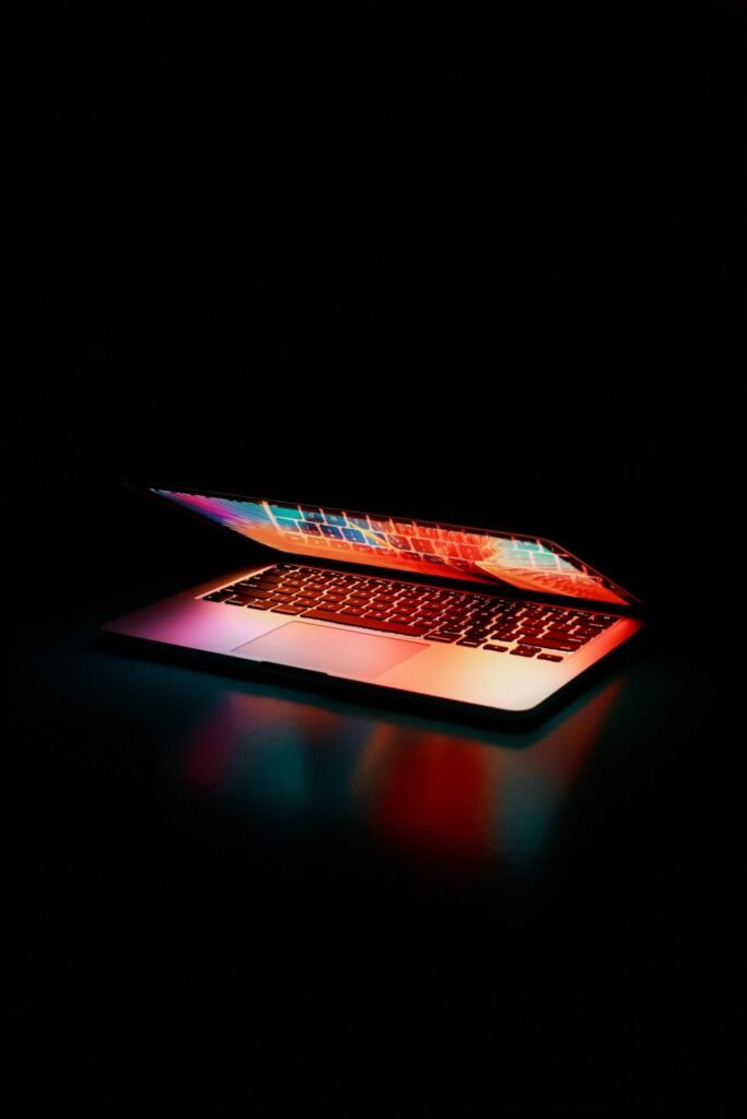 Laptop partially opened, emitting vibrant multicolored lights in dark setting.